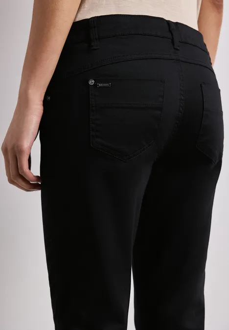 7/8 Slim Legs broek in satijnlook Black Achteraanzicht van een persoon in een zwarte jeans tegen een neutrale achtergrond.