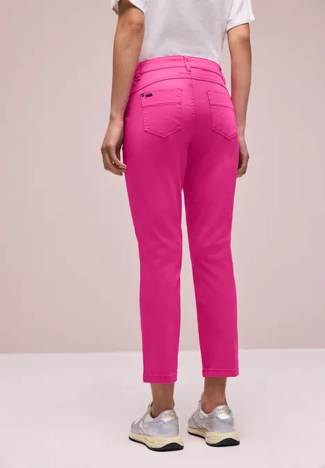 Achteraanzicht van een persoon met knalroze enkellange broek, wit t-shirt en sneakers.