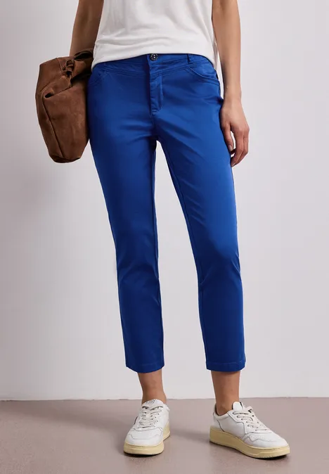 Dame trägt schmale, blaue 7/8-Hose und weiße Sneaker.