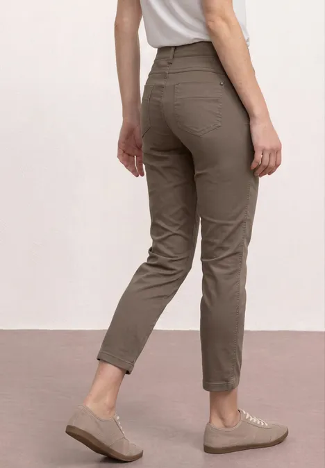 Vrouw van achteren met olijfgroene 7/8-broek en beige sneakers tegen neutrale achtergrond.