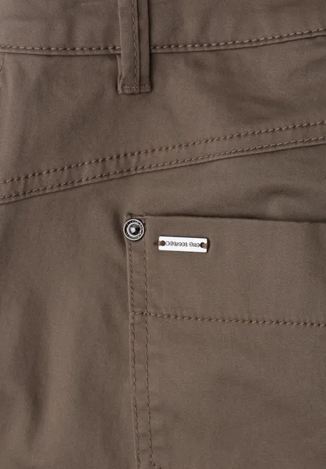 Close-up van een donkerbruine broek met achterzak en klein metalen label.