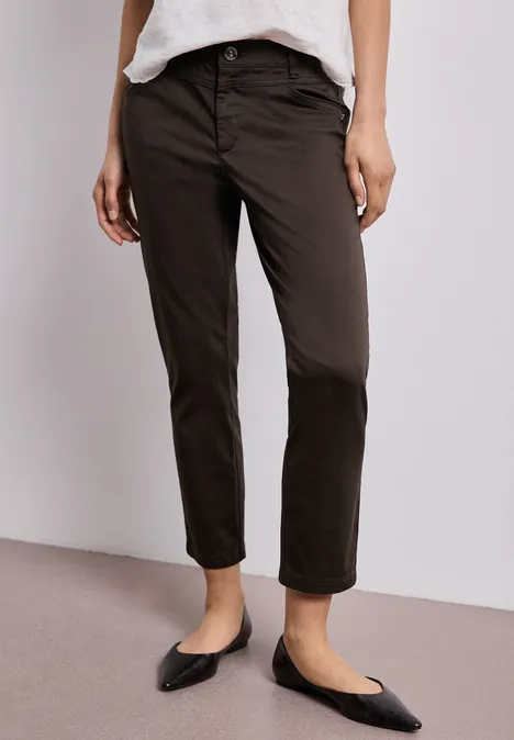 7/8 Slim Legs broek in satijnlook deep earth Vrouw in zwarte 7/8-broek met rechte pijpen en zwarte ballerina’s, tegen lichte achtergrond.