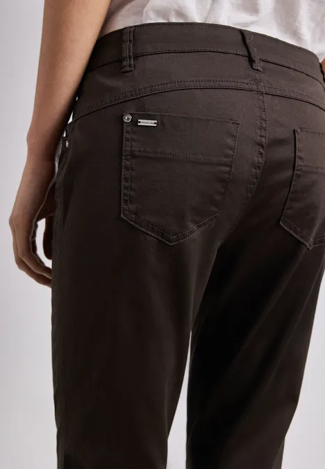 7/8 Slim Legs broek in satijnlook deep earth Achteraanzicht van een persoon in donkerbruine broek met achterzakken en deels zichtbaar wit shirt.