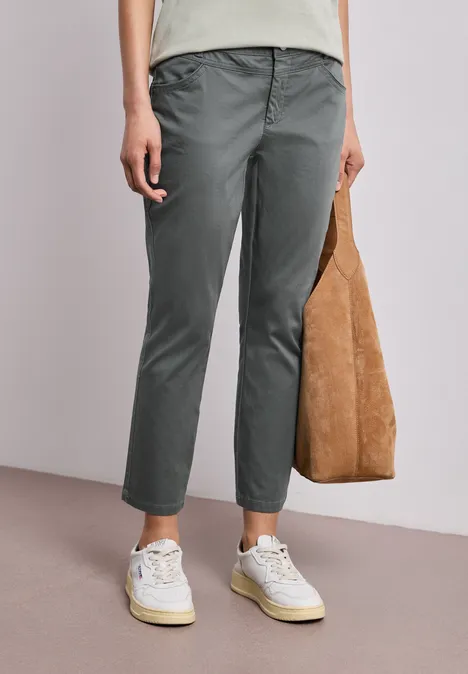 Person trägt graue Chino-Hose, weiße Sneaker und hält eine braune Velours-Ledertasche.