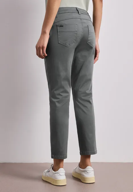 7/8 Slim Legs broek in satijnlook cilantro green Achteraanzicht van een persoon in grijze broek en witte sneakers.