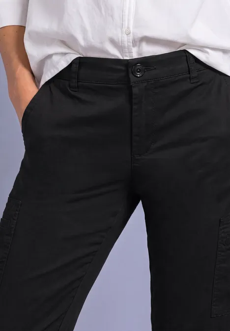 Slim Leg Chino mit Taschen im Cargo-Look Black Modell trägt schwarze Cargohose und weißes Hemd, Hände locker in den Taschen.