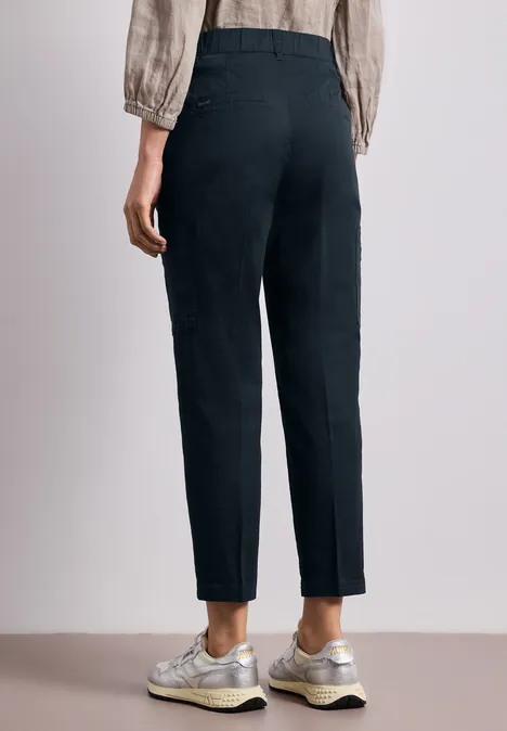 Chino's met Slim Legs en cargo-stijl zakken deep blue Een persoon van achteren draagt een zwarte, hoog getailleerde broek en lichte sneakers, minimalistische achtergrond.