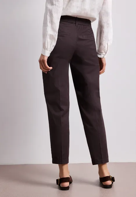 Achteraanzicht van een persoon met wit shirt, donkerbruine taps toelopende broek en zwarte sandalen.