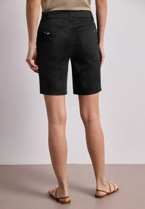 Rückansicht einer Person in schwarzen Bermudashorts und Sandalen auf hellem Boden.