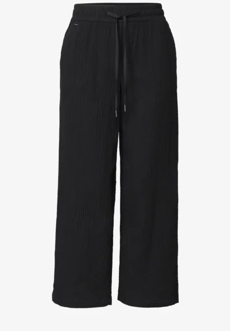 Schwarze, weit geschnittene Hose mit Elastikbund und Kordelzug, strukturierter Stoff, gerade Beinform.