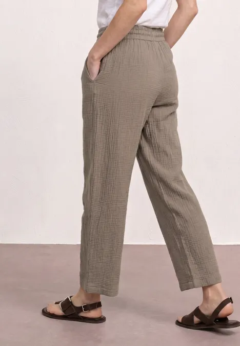 Zijaanzicht: losse, enkelhoge broek in licht olijfgroen met zijzakken en zwarte sandaaltjes.