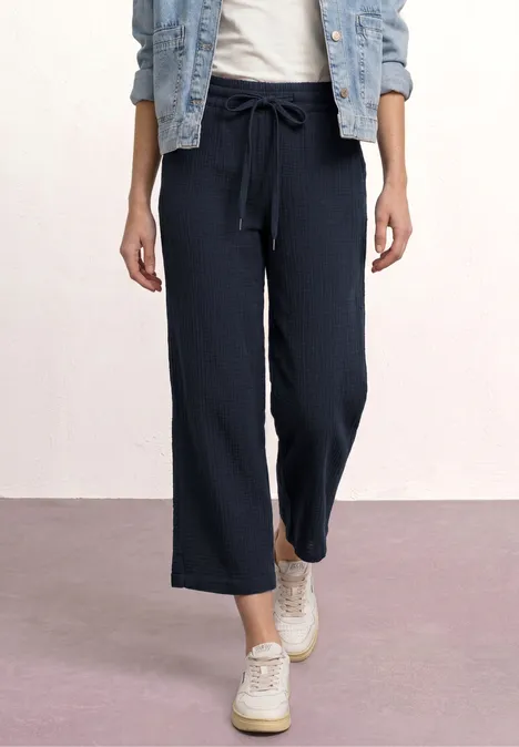 Frau trägt dunkelblaue, hosenbeinweite Hose mit Tunnelzug, Jeansjacke und weiße Schuhe