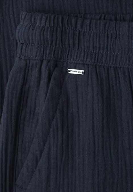 Dunkelblauer, leicht strukturierter Stoff mit elastischem Bund, seitlicher Tasche und kleiner Metallplakette