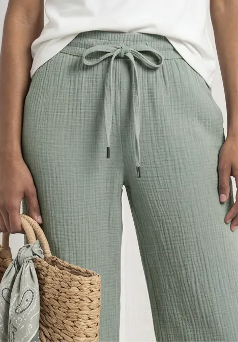 Vrouw met lichtgroene, losse katoenen broek met trekkoord en een gevlochten strooien tas.