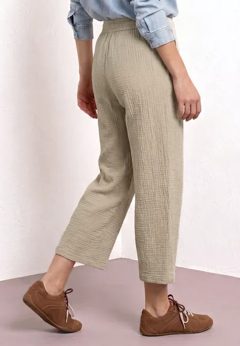 Hellebeige, hoch geschnittene Hose mit weitem Bein bis knapp über den Knöchel, kombiniert mit braunen Schnürschuhen.