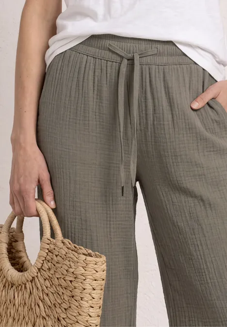 Person trägt locker sitzende, khakigrüne Leinenhose mit Tunnelzug und weißes Top, hält Flechtkorb