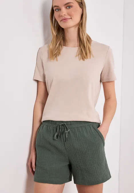 Eine Frau trägt ein beiges T-Shirt und grüne, lockere Shorts mit Tunnelzug.