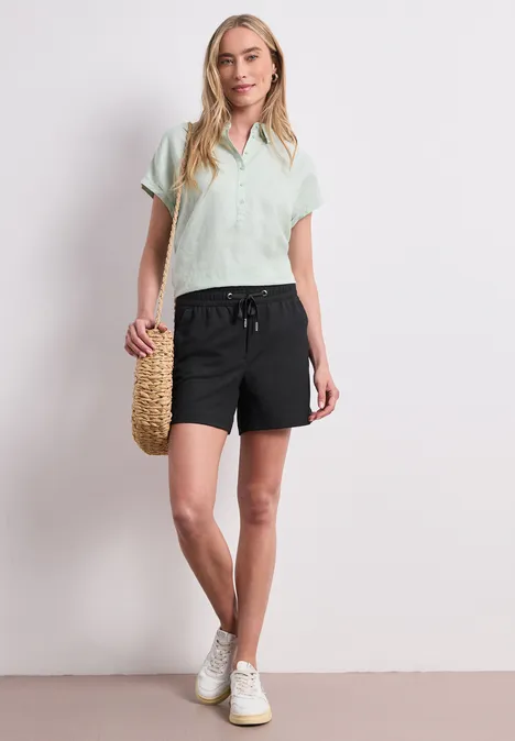 Frau in mintgrünem T-Shirt, schwarzen Shorts und weißen Sneakers, hält einen Bastkorb.