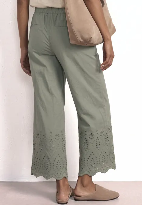 Achteraanzicht van een vrouw in wijde, groene culotte met laser-cut zoom, met tas en comfortabele schoenen.