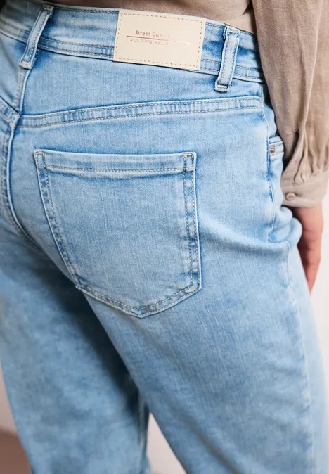 Achteraanzicht van persoon in lichtblauwe spijkerbroek, zichtbare achterzak en taillelabel.