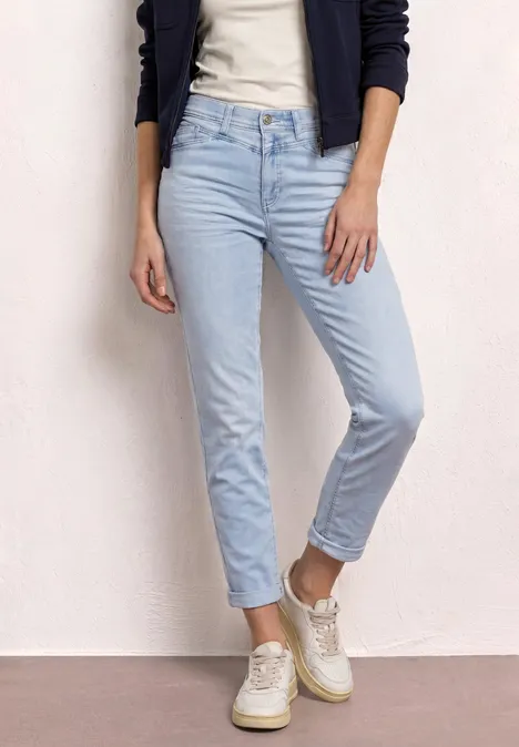 Persoon draagt lichtblauwe jeans, witte sneakers, een t-shirt en een donkerblauwe vest.