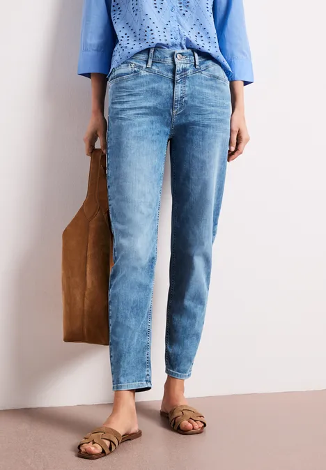 Person trägt helle Denim-Jeans, blaue Bluse, braune Sandalen und hält eine braune Einkauftasche.