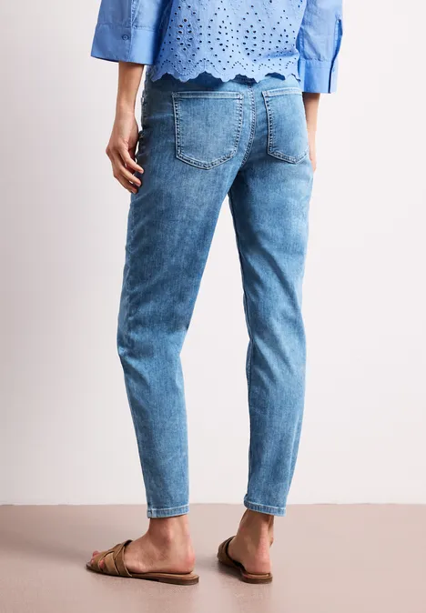 Rückansicht einer Frau in hellblauen Jeans, kombiniert mit einem gehäkelten Oberteil und flachen Sandalen.