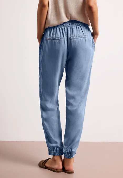 Rugaanzicht van een persoon in lichtblauwe joggingsbroek met elastische taille en sandalen.