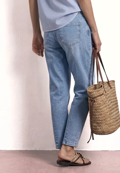 High Waist Barrel Leg Jeans im Loose Fit authentic light blue Eine Person in hellen Jeans und Sandalen hält eine geflochtene Strohhandtasche vor einer weißen Wand.