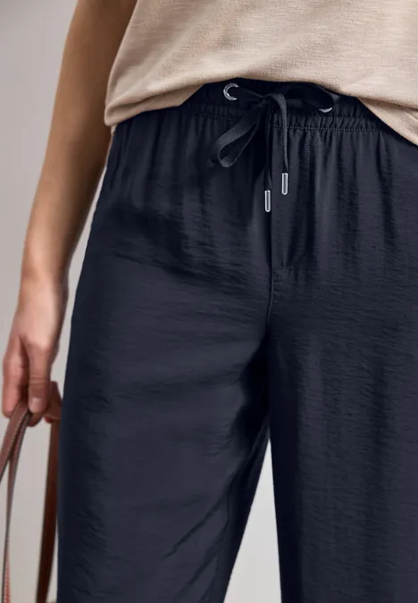 Person trägt schwarze, lässige Hose mit Tunnelzug und hält eine Tasche