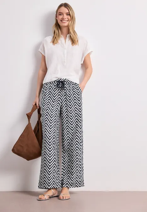 High Waist Wide Leg Hose im Loose Fit deep blue Frau in weißer Bluse und schwarz-weißer Zickzack-Hose mit Schultertasche und Sandalen.