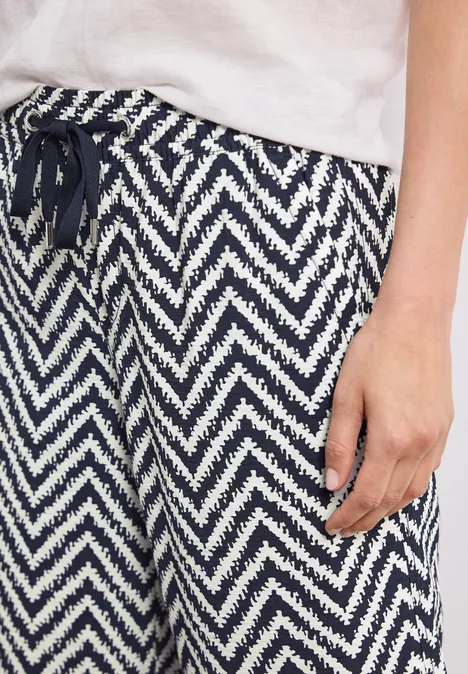 High Waist Wide Leg Hose im Loose Fit deep blue Nahaufnahme einer Person in weißem T-Shirt und blau-weißer Zickzackhose mit Tunnelzug.