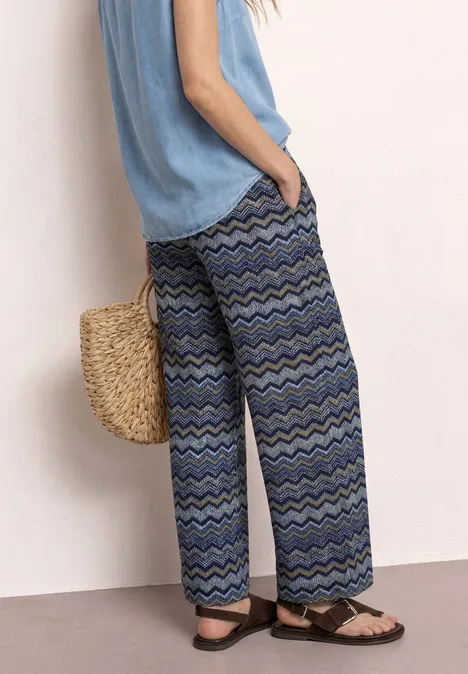 High Waist Wide Leg Hose im Loose Fit frozen wave Weite, blaue Hosen mit Zickzack-Muster, dazu lockeres Top, Strohtasche und Sandalen.