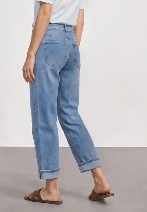 Straight Leg Jeans im Casual Fit mit Turn-Up Light Blue Random Washed Frau in hellblauen, hochgekrempelten Jeans, weißem Oberteil und braunen Sandalen, seitliche Ansicht.