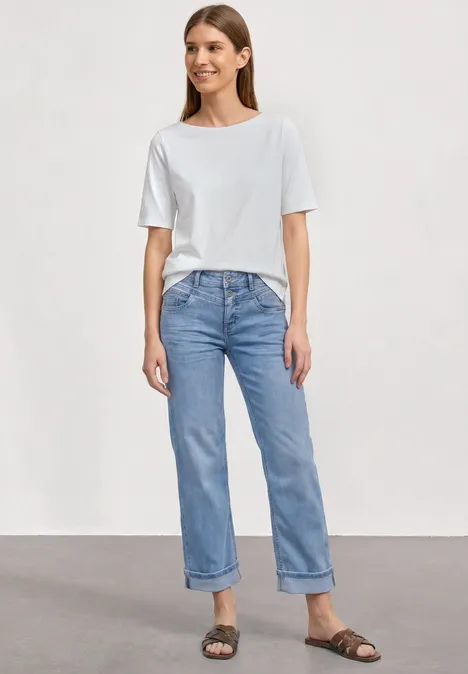 Straight Leg Jeans im Casual Fit mit Turn-Up Light Blue Random Washed Frau trägt weißes T-Shirt, hellblaue, hochgekrempelte Jeans und braune Sandalen, steht vor neutralem Hintergrund.