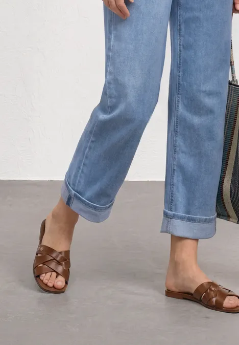 Straight Leg Jeans im Casual Fit mit Turn-Up Light Blue Random Washed Füße in braunen, geflochtenen Ledersandalen und hochgekrempelten, hellblauen Jeans.
