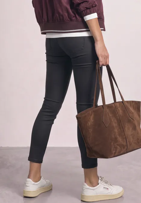 Pantalon taille mi-haute, coupe slim, aspect cuir Black Femme de dos en jean skinny noir, veste bordeaux, baskets blanches, portant un grand sac en daim marron.