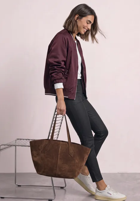 Pantalon taille mi-haute, coupe slim, aspect cuir Black Une femme porte un bomber bordeaux, un jean noir, des baskets blanches et un grand sac en daim marron.