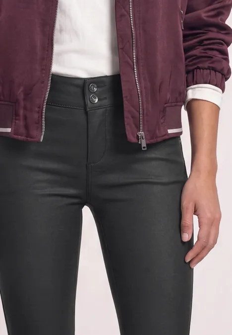 Pantalon taille mi-haute, coupe slim, aspect cuir Black Femme en jeans taille haute noir à double bouton, t-shirt blanc et veste bordeaux, main posée sur la cuisse.