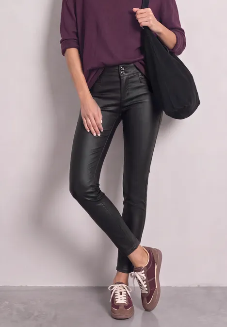 Frau in violettem Shirt, schwarzen Lederleggings und braunen Sneakern, lässig mit Shopper.