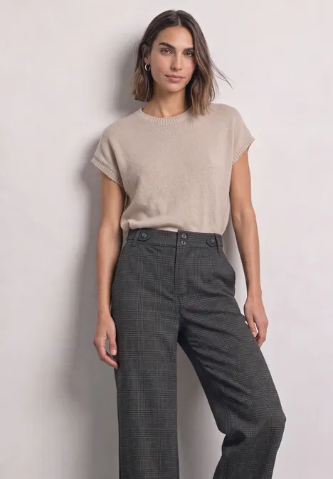 Frau trägt beiges T-Shirt und weite dunkelgraue High-Waist-Hosen vor hellem Hintergrund.