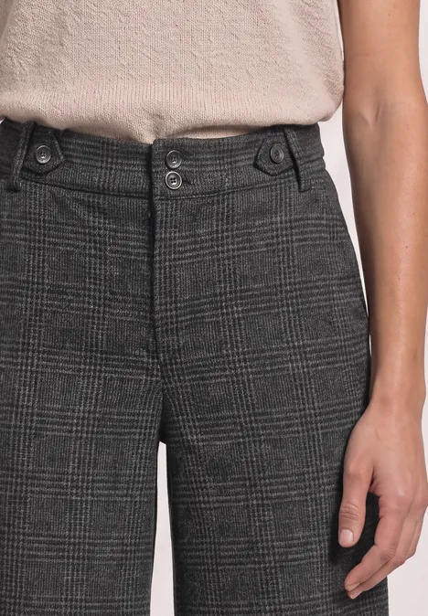 Person trägt graue Karohose mit doppeltem Knopfverschluss und beiges Oberteil.