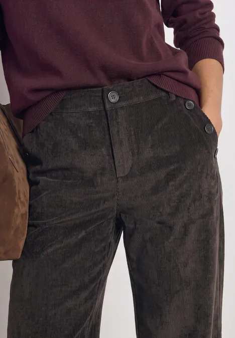 Dunkle Cordhose mit Knopfleiste, kombiniert mit einem kastanienbraunen Pullover.