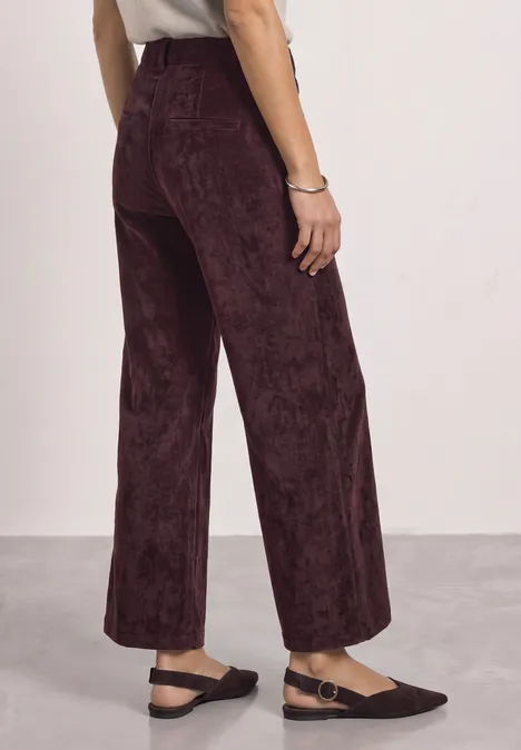 Rückansicht einer Frau in weinroter Cordhose mit weitem Bein und schwarzen Ballerinas.