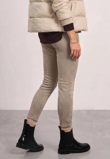 Person trägt beiges Slim-Fit-Hosen-Outfit, schwarze Stiefeletten und Pufferjacke.