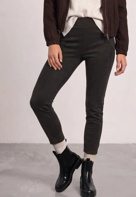 Enge olivgrüne Hose, weiße Socken und schwarze Lederstiefeletten kombiniert mit braunem Blouson.