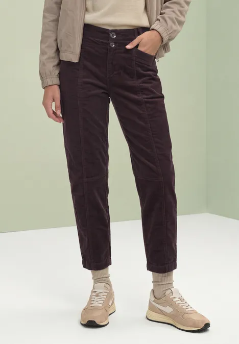 Eine Person trägt dunkle Cordhose und beige Sneaker vor neutralem Hintergrund.