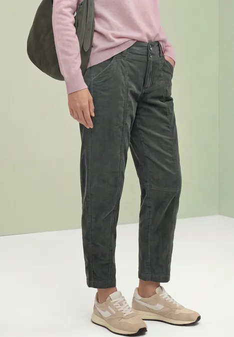 Person trägt pinken Pullover, dunkelgraue Cordhose, beige Sneaker und graue Schultertasche.