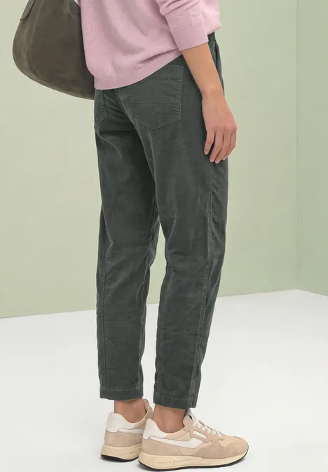 Von hinten: Person trägt graue Cordhose, beigen Sneaker, rosafarbenen Pullover und große Tasche.