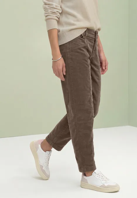 Barrel Leg-broek van corduroy in casual pasvorm velvet mocha Persoon met beige trui, bruine corduroy broek en witte sneakers voor lichte achtergrond.